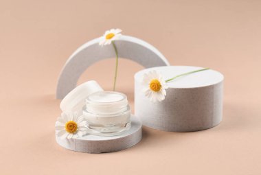 Dekoratif podyumlar bir kavanoz papatya kozmetik kremi ve kahverengi arka planda çiçekler