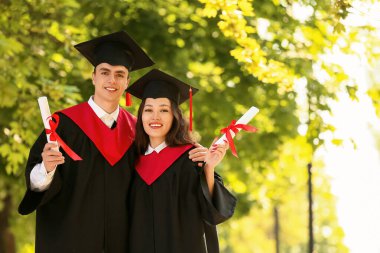 Diplomalı bir çift mutlu mezun öğrenci dışarıda kucaklaşıyor.