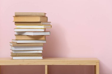 Renk duvarının yanındaki ahşap raf ünitesinde yığınla farklı kitap var.