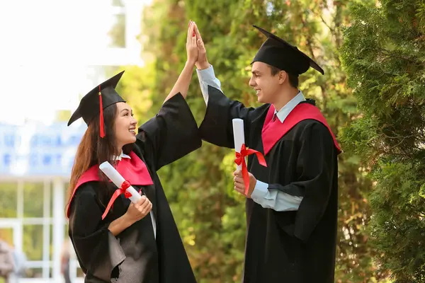 Diplomalı bir çift mezun dışarıda beşlik çakıyor.
