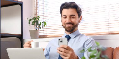 Ofiste cep telefonu kullanan, bilgisayarlı ve kahveli bir iş adamı.