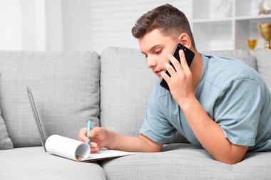 Evde çalışan cep telefonu ve not defteri olan genç bir çocuk.