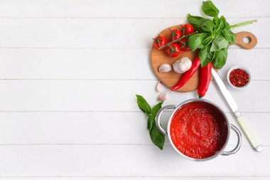 Beyaz ahşap arka planda fesleğen, sarımsak ve biberli domates sosu pişirmek.
