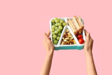Pembe arka planda üzümlü kadın elleri ve okul beslenme çantası.