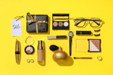 Farklı dekoratif kozmetik ürünleri, hediye kutusu ve sarı arka planda satış etiketleri olan kompozisyon