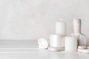Beyaz ahşap arka planda kaplıca taşları, havlu ve bitkisel torba ile mum yakmak