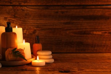 Kaplıca aksesuarları, kozmetik ürünleri ve koyu ahşap arka planda yanan mumlar.