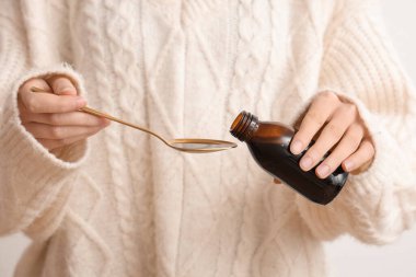 Kadın beyaz arka planda şişeden kaşığa öksürük şurubu döküyor.