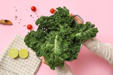 Taze lahana yapraklı süzgeç, limon ve domatesli pembe arka planda kadın elleri.