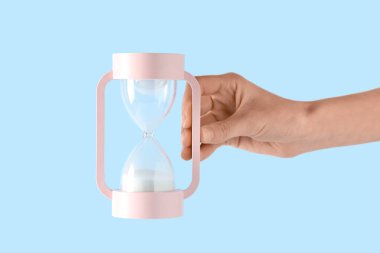 Beyaz kumlu kadın eli mavi arka planda modern kum saati.