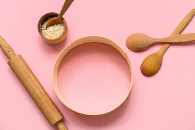 Tahta elek, bir kase un, kaşıklar ve pembe arka planda merdane.