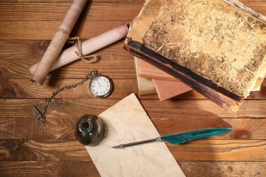 Kağıt çarşaflı eski kitaplar, tükenmez kalem, mürekkep hokkası, parşömenler ve ahşap arka planda cep saati.