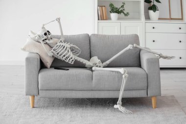 Oturma odasındaki gri koltukta yastıklı insan iskelet modeli.