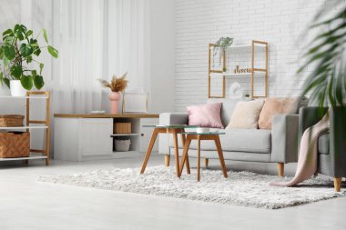 Oturma odasının içinde rahat bir kanepe ve beyaz tuğla duvarın yanındaki masalar.