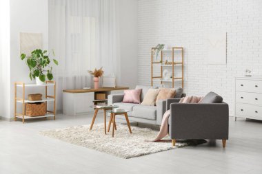 Oturma odasının içinde rahat bir kanepe, koltuk ve beyaz tuğla duvarın yanındaki masalar.