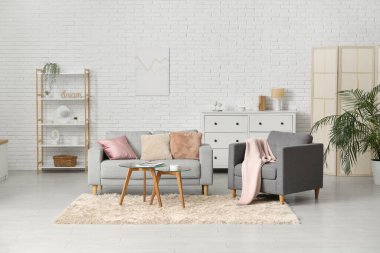 Oturma odasının içinde rahat bir kanepe, koltuk ve beyaz tuğla duvarın yanındaki masalar.