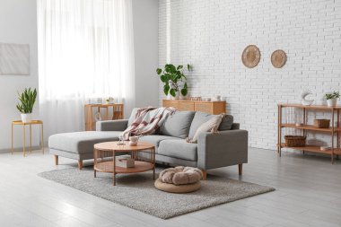 İçinde rahat gri kanepe, puf ve masa olan oturma odası.