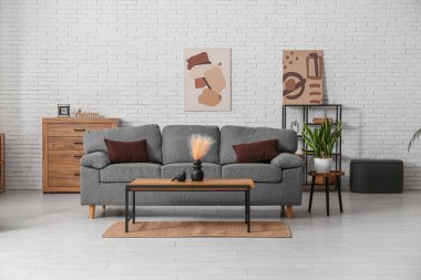 Rahat gri kanepesi ve beyaz tuğla duvarın yanındaki masası olan oturma odasının içinde.