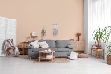 Oturma odasının iç tarafındaki bej duvarın yanında rahat bir kanepe, masa ve dergi tutucusu.