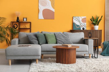 Oturma odasının içinde rahat bir kanepe ve sarı duvarın yanında bir sehpa var.