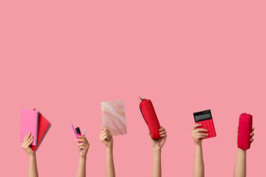 Pembe arka planda farklı kırtasiye malzemesi olan kadın elleri