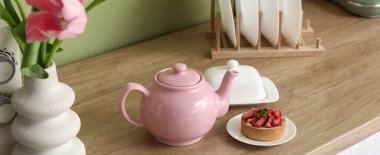 Pembe çaydanlık, lezzetli bir tatlı ve güzel lale çiçekleri mutfaktaki yeşil duvarın yanındaki masada.