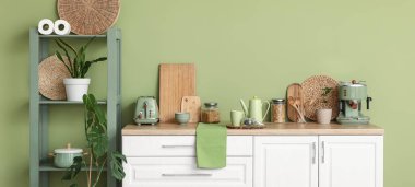 Mutfağın içinde çaydanlık, bir kavanoz kuru çay ve fincanla yeşil duvarın yanında.