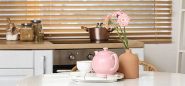 Pembe çaydanlık, bir fincan çay ve mutfaktaki masada güzel çiçekler.