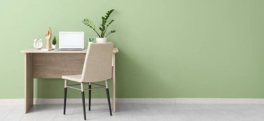 Modern dizüstü bilgisayarı, sandalyesi ve rahat ofisin yeşil duvarının yanındaki bitkisi olan şık bir iş yeri.
