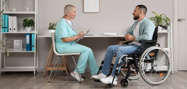 Hastanede tekerlekli sandalyede genç bir adamla çalışan kadın doktor.