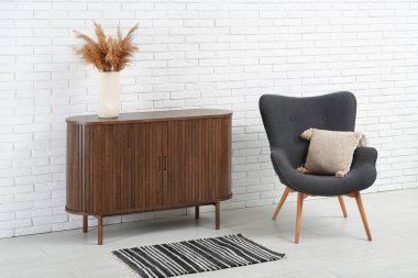 Şık bir koltuk ve hafif tuğla duvarın yanındaki ahşap dolap.