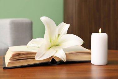 Güzel zambak çiçeği, yanan mum ve kitap odasındaki ahşap masada.