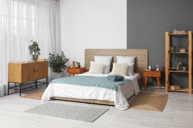 Yatak odasının içinde ahşap yatak, ev bitkileri ve komodinin yanında çalar saat var.