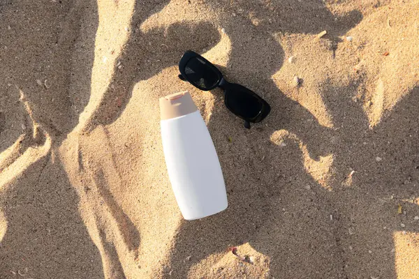 Bir şişe güneş kremi ve kumsalda güneş gözlüğü.