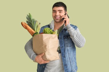 Bakkal çantalı genç adam yeşil arka planda cep telefonuyla konuşuyor.