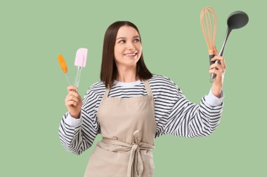 Önlüklü, yeşil arka planda mutfak aletleri olan güzel bir kadın.