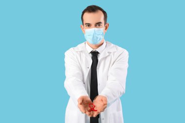 Mavi arka planda kırmızı kurdeleli ve yüz maskeli genç bir erkek doktor. Dünya AIDS Günü konsepti