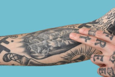 Koluna krem süren bir adam. Mavi arka planda dövmeleri var. Yakın plan.