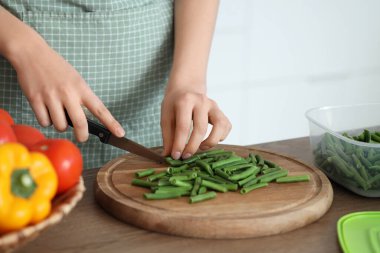 Mutfaktaki ahşap masada donmak için yeşil fasulye kesen kadın, yakın plan.