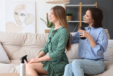 Genç bir kadın arkadaşının saçını evde yapıyor.