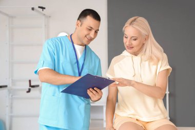 Rehabilitasyon merkezinde panosu olan bir erkek fizyoterapist ve olgun bir kadın.