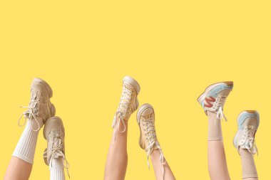 Sarı arka planda farklı spor ayakkabıları olan kadın bacakları.