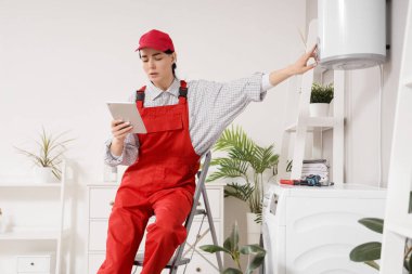 Tablet bilgisayarlı kadın işçi banyoda modern elektrikli kazanı ayarlıyor.