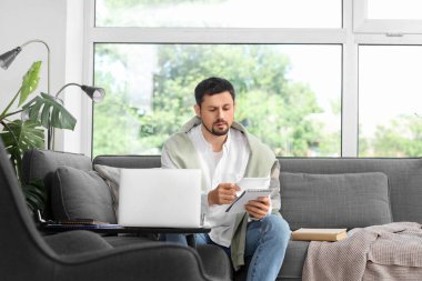 Bilgisayarlı ve defterli kafası karışmış genç erkek öğretmen evde online ders veriyor.