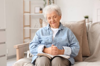 Kanepede oturup İncil okuyan kıdemli bir kadın.