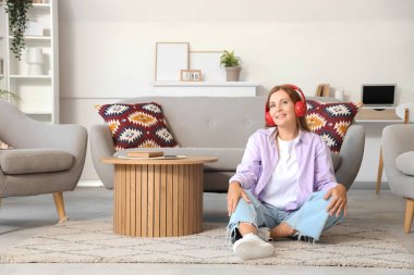 Evde yerde oturan kulaklıklı olgun bir kadın.