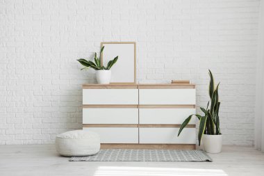 Çerçeveli çekmeceler, ev bitkileri ve oda beyaz tuğla duvarın yanındaki puf.