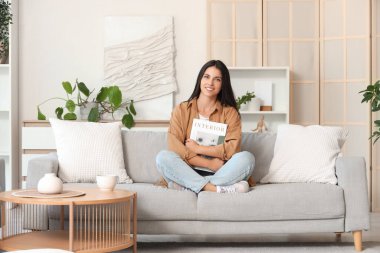 Dergilerle güzel bir kadın sabahları kanepede oturuyor.