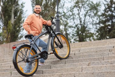 Kulaklığı ve bisikleti olan genç mutlu bir adam şehirde yukarı çıkıyor.