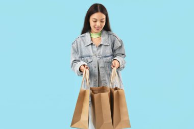 Mavi arka planda alışveriş torbaları olan mutlu genç bir kadın.